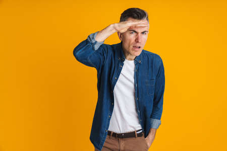 Brooding handsome man posing and looking at camera isolated over yellow background