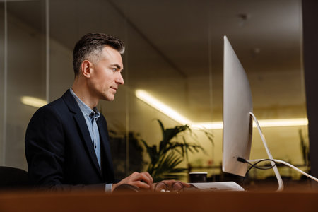 Serious handsome man working with computer while sitting at table in office