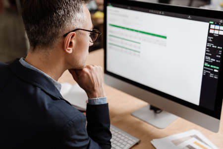 Serious handsome man working with computer while sitting at table in office
