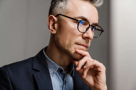 Serious grey man wearing eyeglasses thinking and looking forward in officeの写真素材