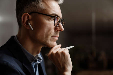 Concentrated grey man in wireless earphones working at officeの写真素材