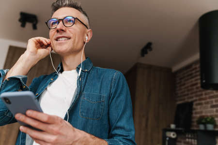 Close up of a smiling man listening to music with earphones at home
