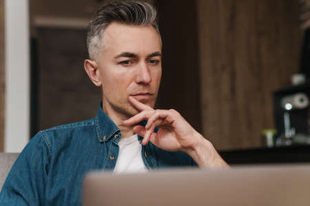 Focused handsome man using laptop while sitting on couch at home