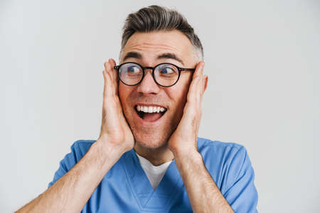 Excited white-haired medical doctor exclaiming and looking aside isolated over white wall