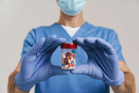 Medical doctor in face mask and gloves showing capsules at camera isolated over white wallの写真素材