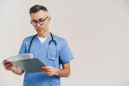 Focused grey doctor with stethoscope examining medical file isolated over white wallの写真素材