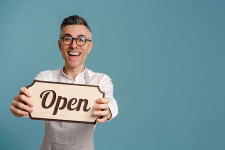 Joyful grey-haired man in eyeglasses smiling and showing banner isolated over blue backgroundの写真素材
