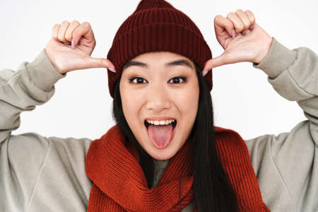 Asian excited nice girl showing her tongue and pointing fingers at her head isolated over white backgroundの写真素材