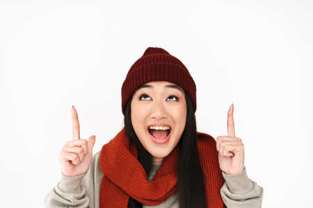 Asian happy nice girl smiling and pointing fingers upward isolated over white backgroundの写真素材