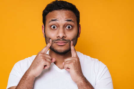 Asian young unshaven surprised man doing smile gesture with fingers isolated over yellow backgroundの写真素材