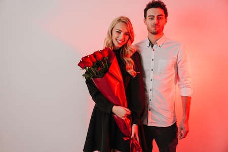 Lovely romantic young happy couple celebrating an event together, woman holding bouquet of red roses isolated over white backgroundの写真素材