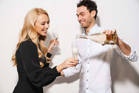Beauitufl young happy smartly dressed couple celebrating Valentines day, drinking champagne isolated over white background, man pouring drinkの写真素材