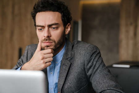 Handsome brooding businessman using laptop while working at homeの写真素材