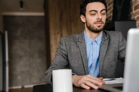 Handsome serious businessman using laptop while working at home
