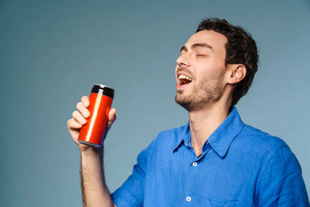 Happy handsome guy drinking soda with eyes closed isolated over blue backgroundの写真素材