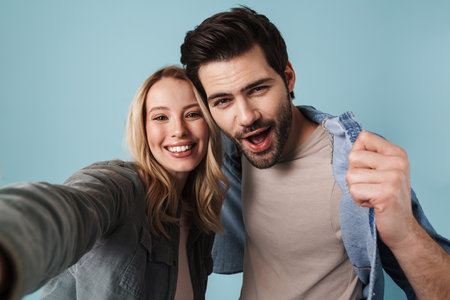 Young excited couple hugging while taking selfie photo isolated over blue backgroundの写真素材