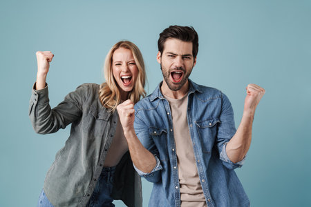 Young excited man and woman screaming and making winner gesture isolated over blue backgroundの写真素材