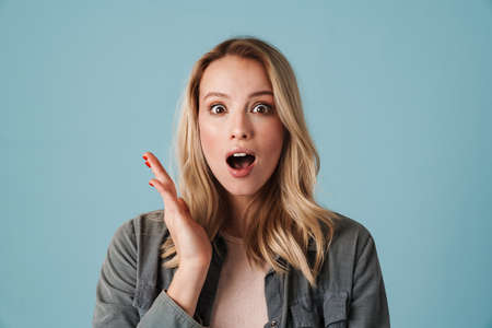 Happy beautiful excited girl expressing surprise and looking at camera isolated over blue background