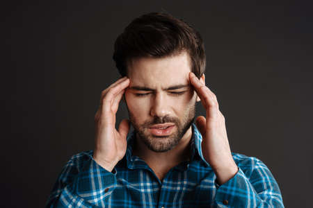 Unhappy handsome unshaven guy with headache rubbing his temples isolated over black backgroundの写真素材
