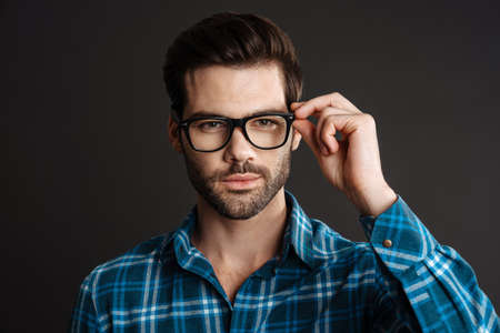 Confident brutal guy in eyeglasses posing on camera isolated over black backgroundの写真素材