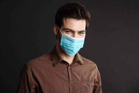 Pleased handsome young man posing in protective mask isolated over black backgroundの写真素材