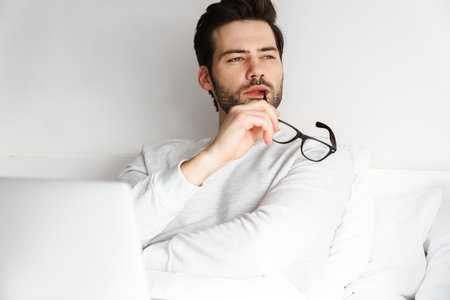 Focused handsome man using laptop while resting in bed at homeの写真素材