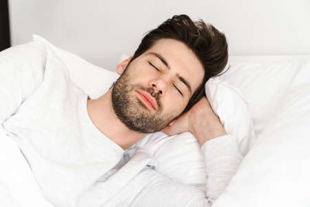 Peaceful handsome young man sleeping and resting in bed at home
