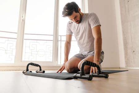 Focused athletic man doing exercise with push-up stops while working out at home