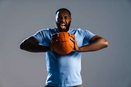 Young african basketball player with basketball during game isolated over gray backgroundの写真素材