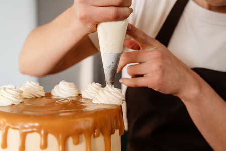 Focused baker woman making cake with cream in kitchen at homeの写真素材