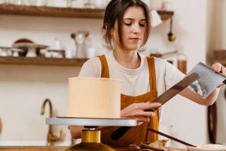 Beautiful concentrated pastry chef woman making cake with cream at cozy kitchenの写真素材