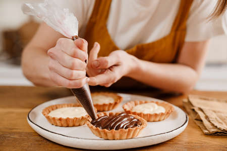 Caucasian pastry chef woman making tarts with cream at cozy kitchenの写真素材