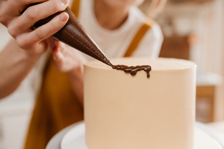 Caucasian pastry chef woman making cake with chocolate cream indoorsの写真素材