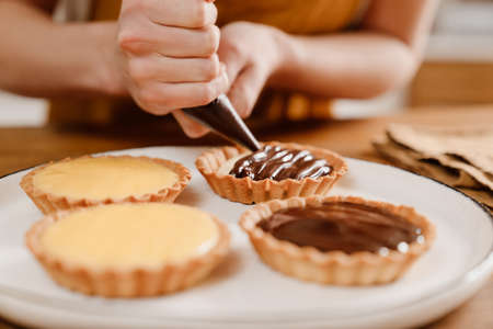 Caucasian pastry chef woman making tarts with cream at cozy kitchenの写真素材