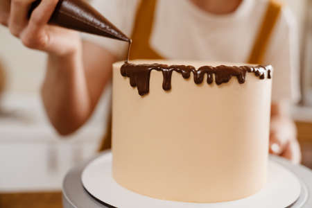 Caucasian pastry chef woman making cake with chocolate cream indoorsの写真素材