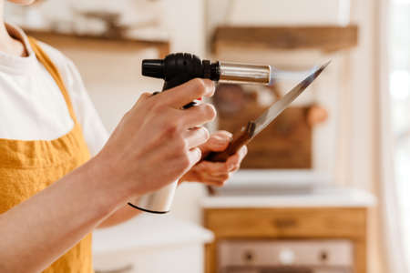 Caucasian pastry chef woman heating knife with gas burner at cozy kitchenの写真素材