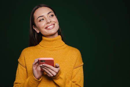 Happy beautiful girl smiling and using mobile phone isolated over green background