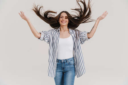 Joyful beautiful brunette girl smiling and making fun with hair isolated over white backgroundの写真素材