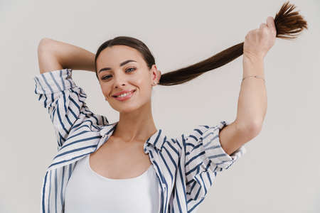 Joyful beautiful brunette girl smiling and making fun with hair isolated over white backgroundの写真素材
