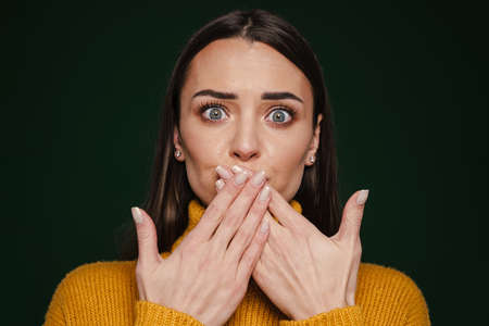 Shocked beautiful girl expressing surprise and covering her mouth isolated over green background