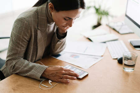 Serious charming woman using cellphone while working with computerの写真素材