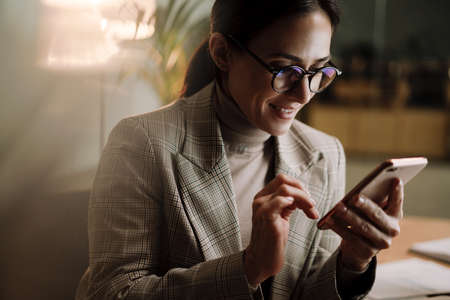 Happy charming woman using cellphone while working in officeの写真素材