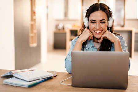 Happy beautiful woman in headphones smiling while using laptop at home