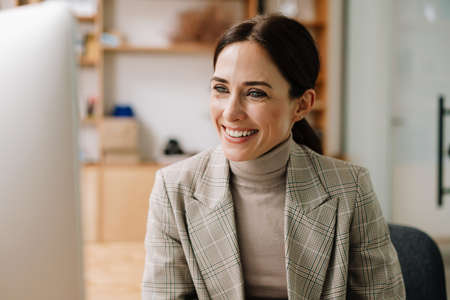 Happy charming woman smiling while working with computer in officeの写真素材