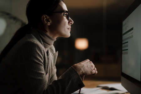 Focused charming woman in eyeglasses working with computer while sitting in office
