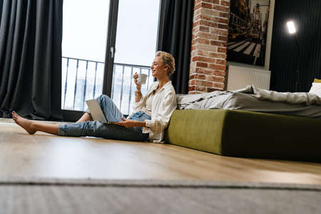 Smiling young woman on a video call through laptop computer while leaning on a couch at home