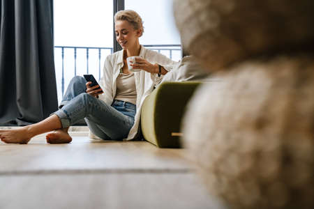 Woman relaxing while leaning on a sofa, using smartphone at home