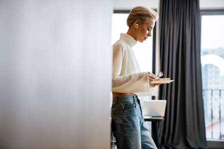Attractive young woman having conversation via earphones during her lunch at home