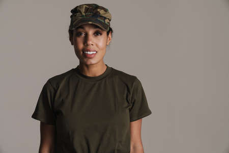 Happy african american soldier woman smiling and looking at camera isolated over grey wall