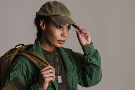 Confident african american soldier woman posing with backpack isolated over grey wallの写真素材